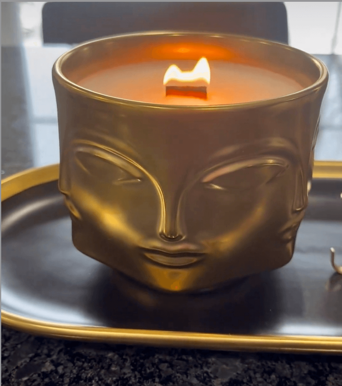 Stay Golden candle in a unique, golden face-shaped holder, evoking the scent of citrus, gardenia, coconut, amber, vanilla, and musk.