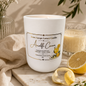 A white scented candle jar labeled 'Anaffic Cream' by Sweet Escape Luxury Candles, styled on a marble board with lemon slices, a beige cloth, and greenery in a warm, clean setting.